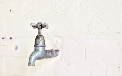A basin wrench positioned under a kitchen sink reaching up to tighten a faucet mounting nut