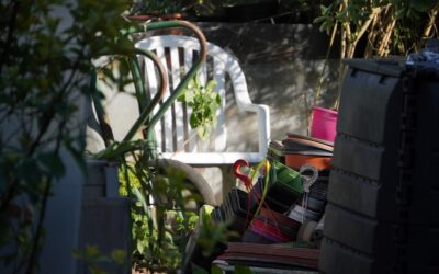 A black tumbler compost bin in a sunny backyard garden next to raised vegetable beds