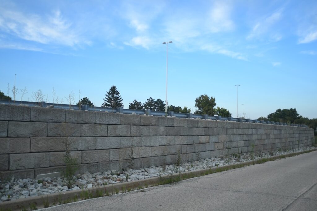Stack of gray cinderblocks on a construction site with a partially built retaining wall in the background