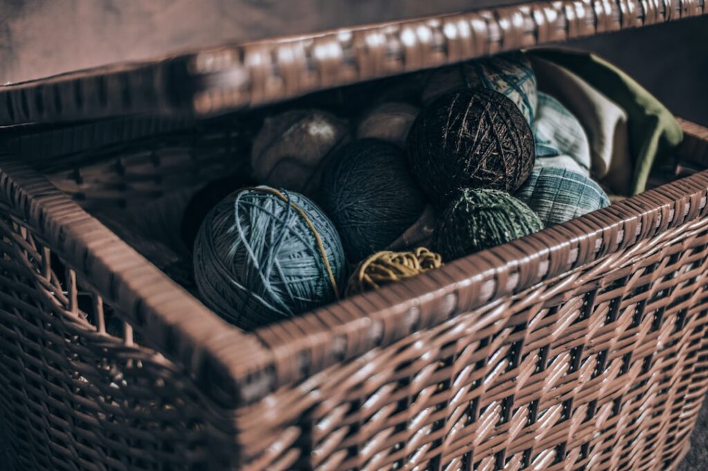 Several white wool dryer balls sitting in a woven laundry basket next to folded towels