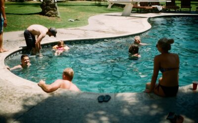 Two adults relaxing on colorful inflatable pool floats in a backyard swimming pool
