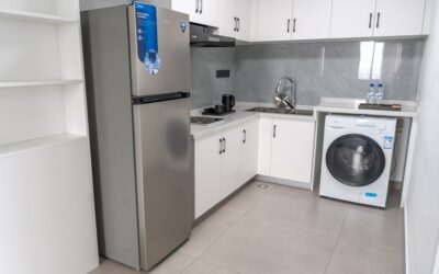 Compact portable washing machine on kitchen floor next to a sink hookup in a small apartment