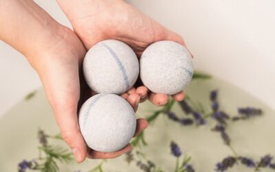 Six white wool dryer balls sitting in a laundry basket next to folded towels