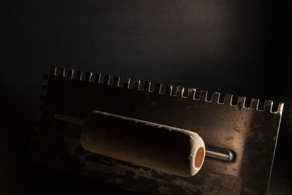 Applying mastic tile adhesive to a wall with a notched trowel before setting ceramic tile